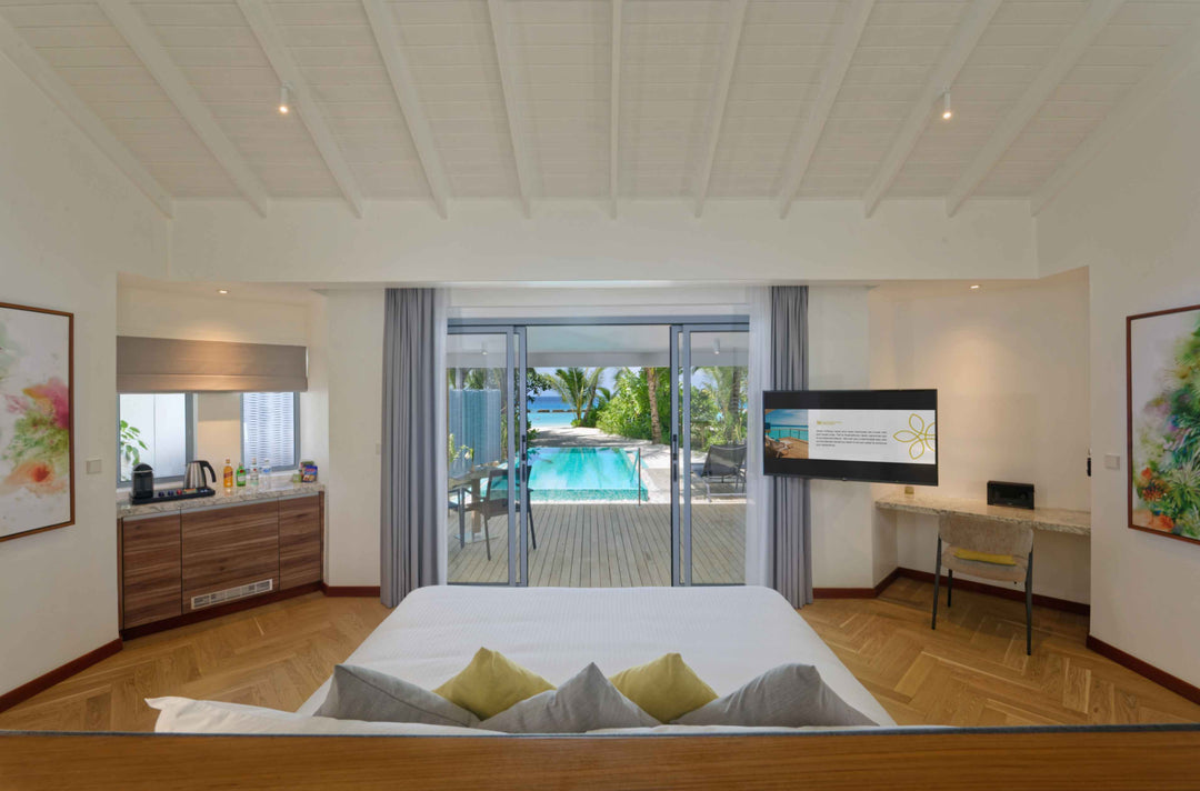 Beach villa bedroom opening through sliding doors onto a deck and private pool