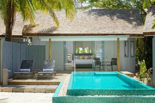 Beach villa with a turquoise private pool, sun loungers and palms overhead