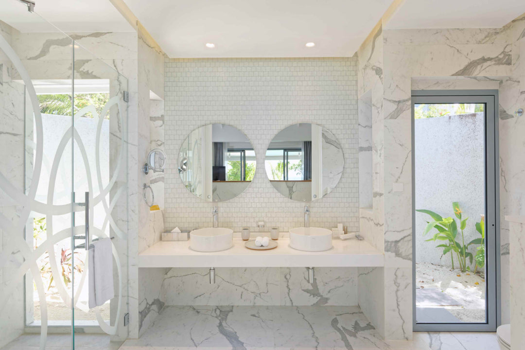 Beach villa bathroom in white marble with twin basins and a glazed outdoor shower