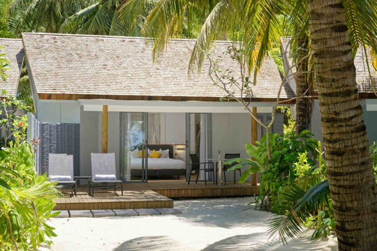 Beach villa seen from the sand, its bedroom open to a deck under coconut palms