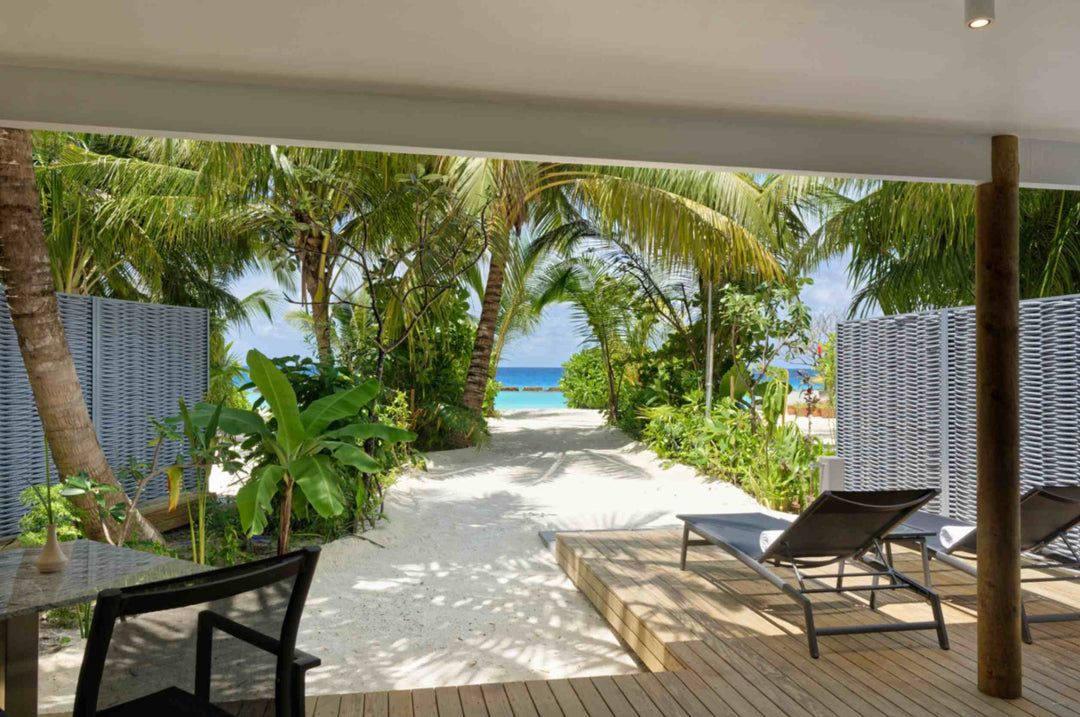 Shaded beach villa deck with sun loungers, looking through the garden out to the sea