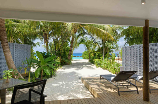 Shaded beach villa deck with sun loungers, looking through the garden out to the sea