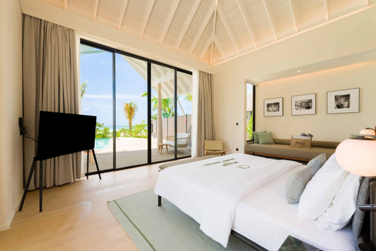 A Beach Pool Villa bedroom at ananea Madivaru Maldives, the pool and palms through the glazed wall