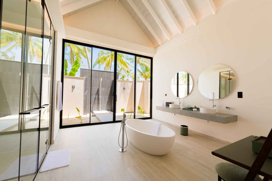 A villa bathroom at ananea Madivaru Maldives, freestanding bath under twin round mirrors beside a planted outdoor shower