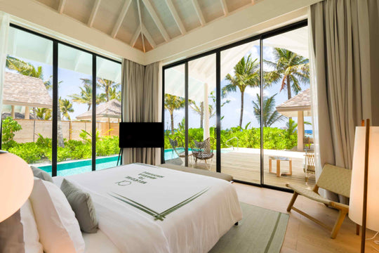A Deluxe Beach Pool Villa bedroom at ananea Madivaru Maldives, the bed facing glass doors on to the pool and the garden