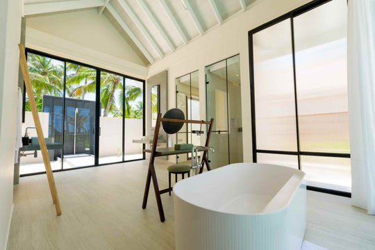 A villa bathroom at ananea Madivaru Maldives under a pitched ceiling, freestanding bath beside a ladder rail