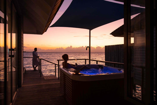 Two guests at sunset on an over-water deck, one relaxing in the villa&