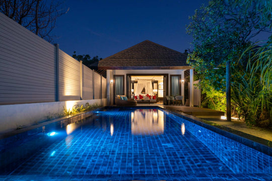 Atmosphere Kanifushi, Lhaviyani Atoll — Kanifushi Beach Villa with Pool after dark: the pool lit blue between timber privacy walls, the villa doors folded open on to a lit lounge.