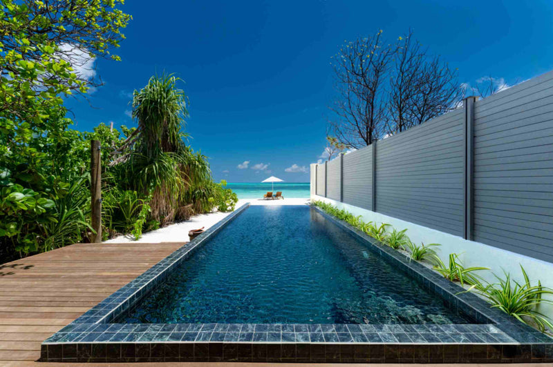 The pool of a Kanifushi Beach Villa with Pool at Atmosphere Kanifushi running from the deck towards the beach, with sun loungers and a parasol on the sand beyond.