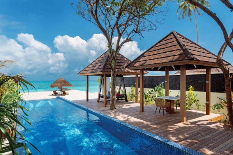 The pool of a Kanifushi Grand Pool Villa at Atmosphere Kanifushi, with two timber salas and a garden swing beside it and the lagoon just beyond.