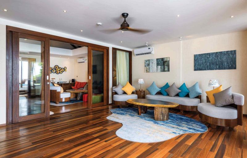 The entertainment room of the Kanifushi Residence at Atmosphere Kanifushi, sofas with coloured cushions around a low table, double doors open through to the next room.