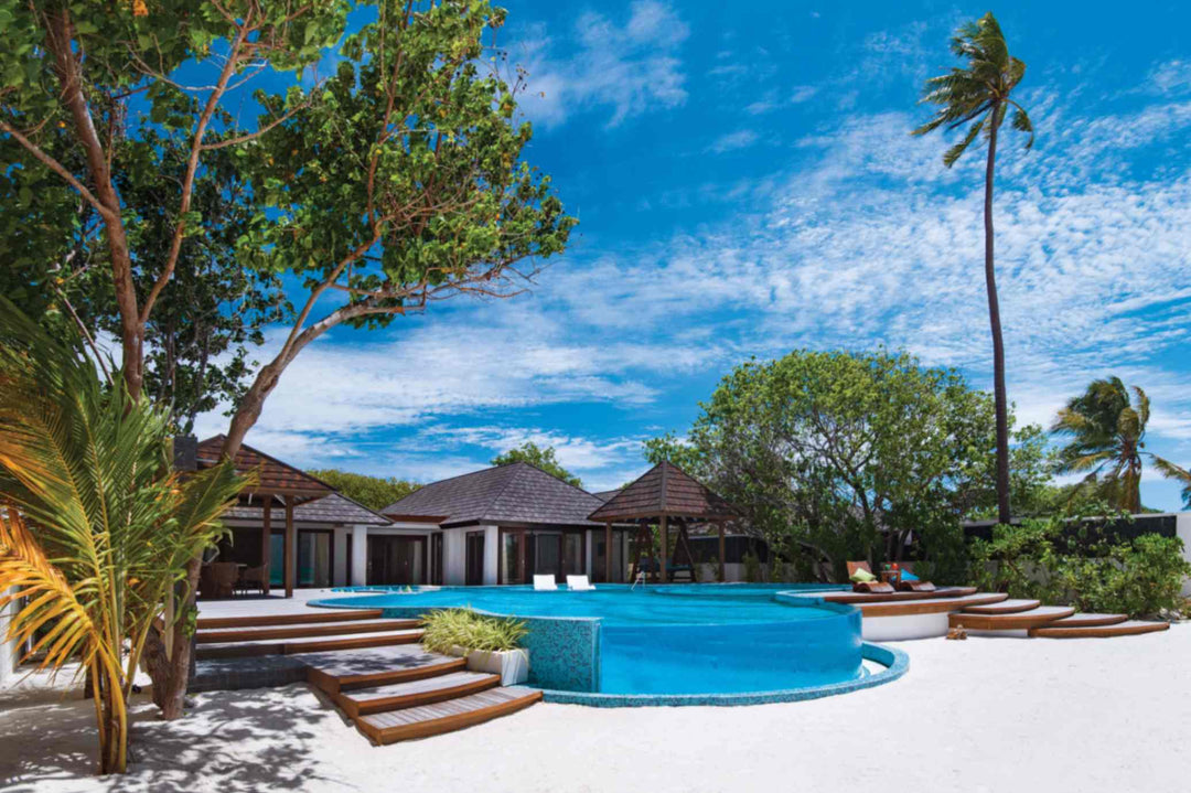 Atmosphere Kanifushi, Lhaviyani Atoll — the Kanifushi Residence from outside: pitched-roof pavilions behind a large private pool with sun loungers, framed by palms.
