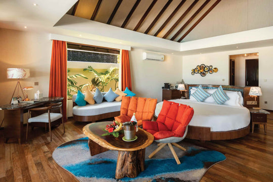 Atmosphere Kanifushi, Lhaviyani Atoll — the master bedroom of the Kanifushi Residence, bed with orange cushions, writing desk, and a day bed at a window on to the garden.