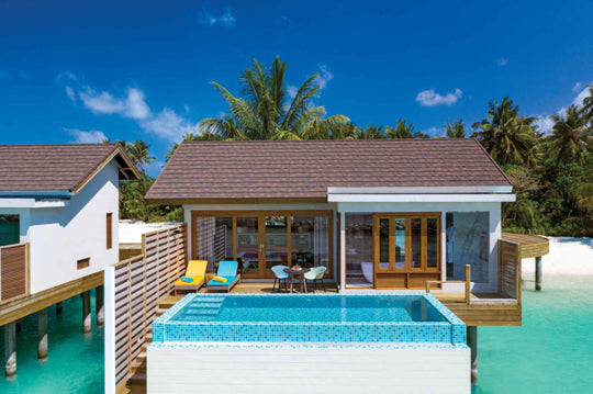 Atmosphere Kanifushi, Lhaviyani Atoll — a Sunset Water Villa with Pool on stilts over the lagoon, sun loungers on the deck beside its plunge pool and the beach behind.