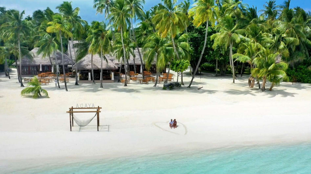 A wooden arch standing on the white sand beach at Ayada Maldives, palms leaning over the shore