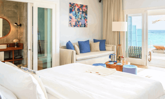 A Sunset Water Pool Villa bedroom at Amilla Maldives, blue cushions and doors open to the water