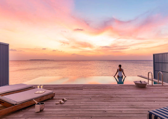 A guest on the villa deck at Amilla Maldives watching a pink sunset over the lagoon