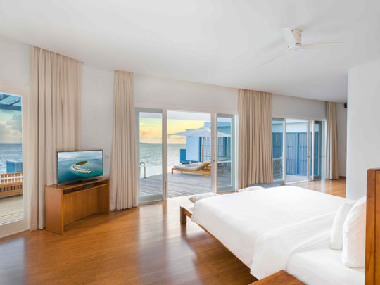 A Lagoon Water Pool Villa bedroom at Amilla Maldives, looking out through open doors to the lagoon