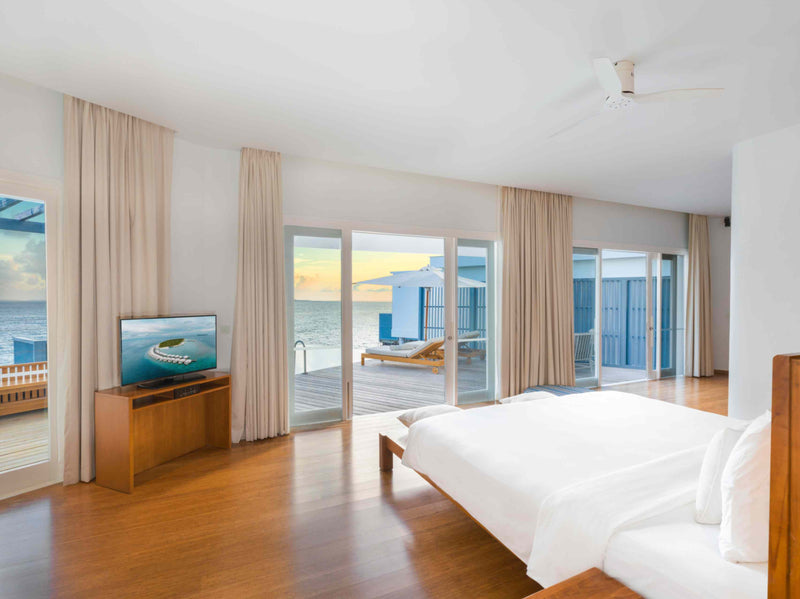 A Lagoon Water Pool Villa bedroom at Amilla Maldives, looking out through open doors to the lagoon