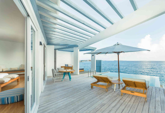 The deck of a Lagoon Water Pool Villa at Amilla Maldives, parasol and loungers above the water