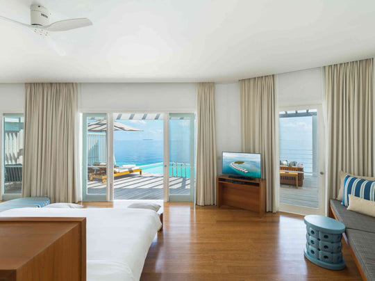 A Reef Water Pool Villa bedroom at Amilla Maldives, curtains drawn back to the lagoon