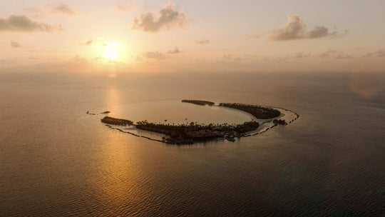 The sun low over ananea Madivaru Maldives, the island a dark outline on still water