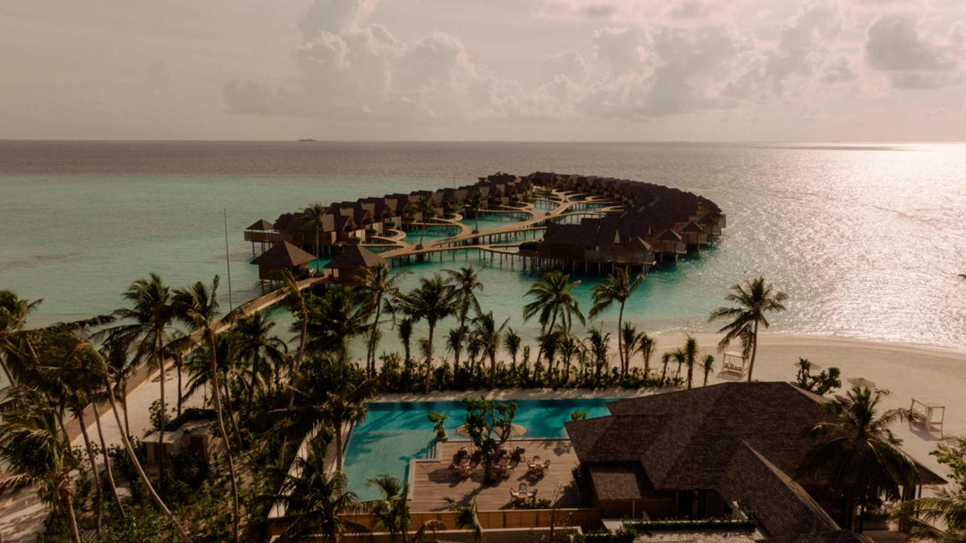 ananea Madivaru Maldives from the air at dusk, the overwater villas reaching out from the palms