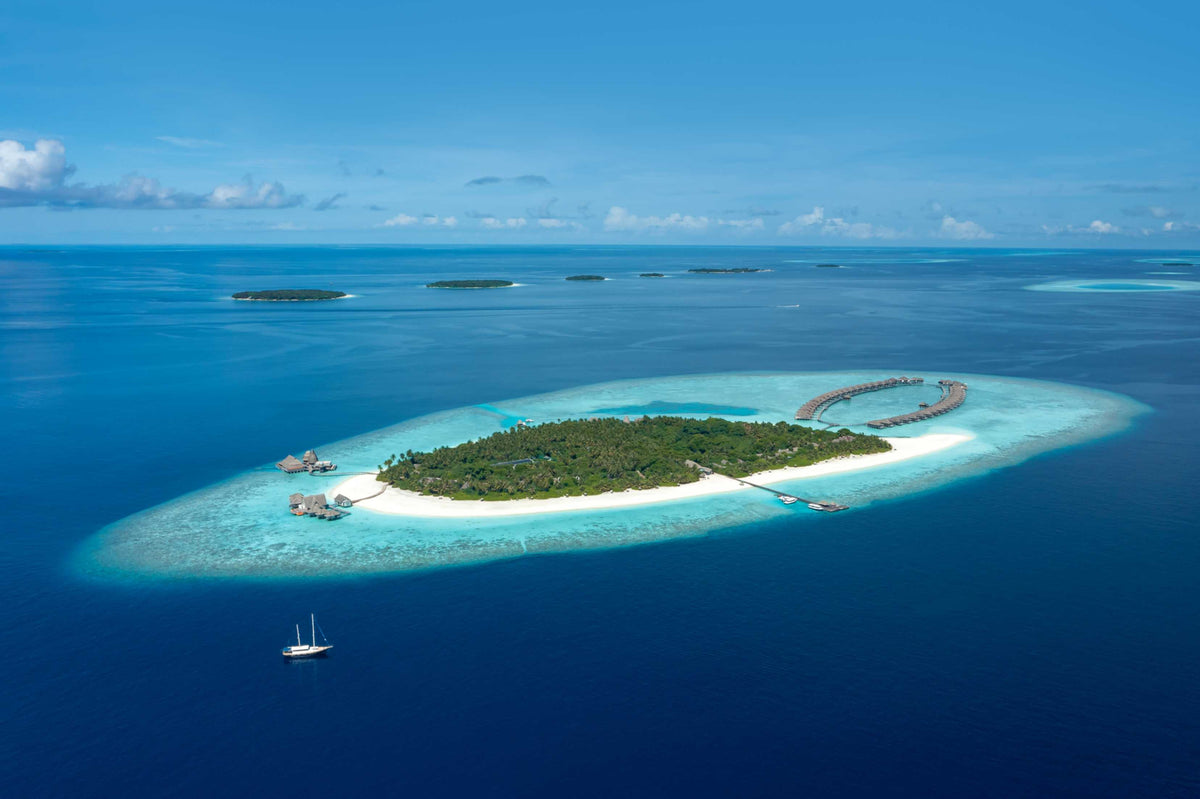 Anantara Kihavah Maldives Villas seen from a distance, the wooded island ringed by its reef