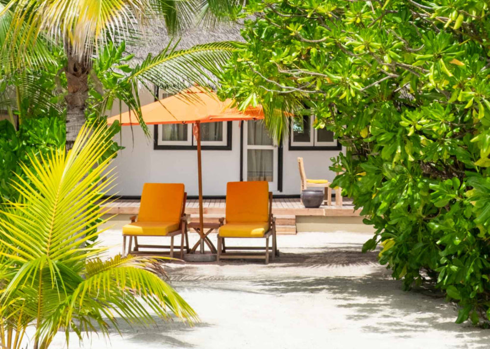 Angsana Velavaru, Dhaalu Atoll — orange sun loungers and a parasol on the sand outside a beachfront villa, screened by dense greenery