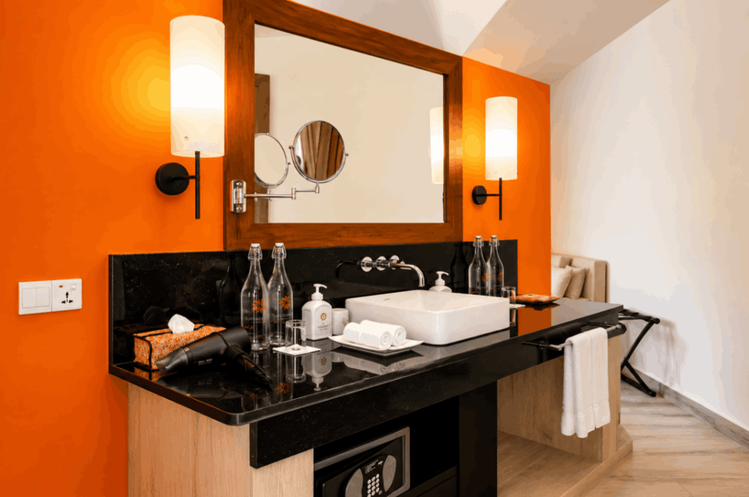 Angsana Velavaru, Dhaalu Atoll — villa vanity with a stone counter and twin mirrors against an orange wall