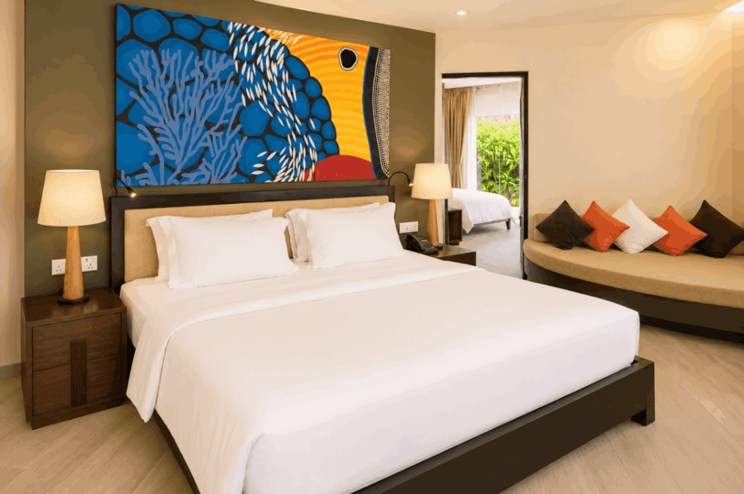 Angsana Velavaru, Dhaalu Atoll — beachfront family villa bedroom with blue coral artwork above the bed and a daybed under the window
