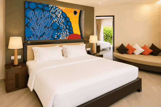 Angsana Velavaru, Dhaalu Atoll — beachfront family villa bedroom with blue coral artwork above the bed and a daybed under the window