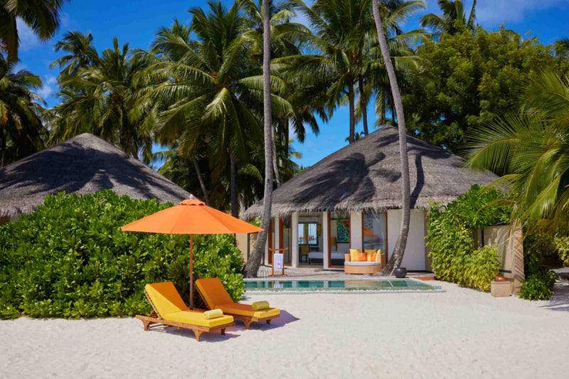 Two thatched beachfront villas at Angsana Velavaru side by side, with a shared pool and loungers on the sand.