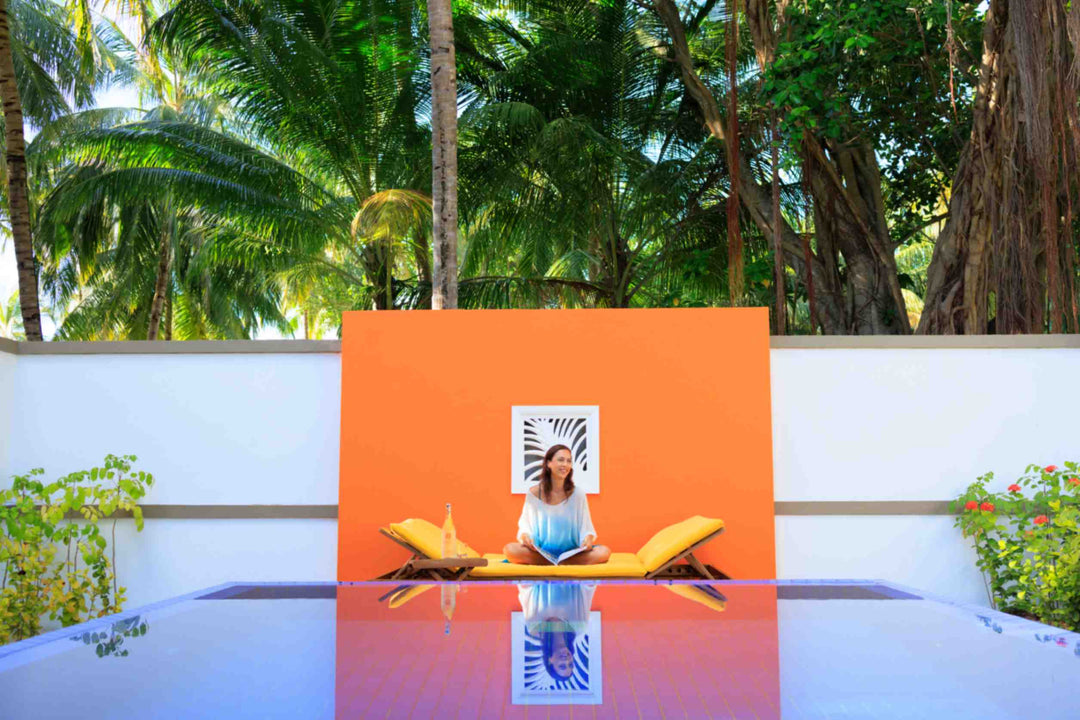Angsana Velavaru, Dhaalu Atoll — a guest sitting on the loungers beside the villa pool, against an orange wall