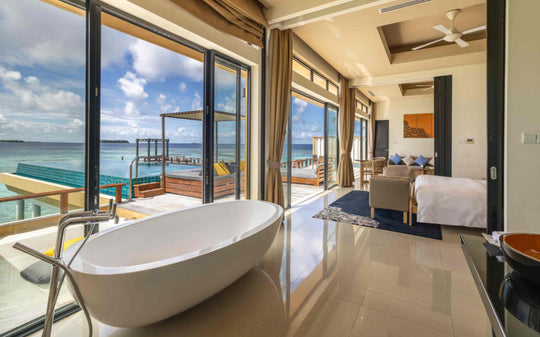 Angsana Velavaru, Dhaalu Atoll — freestanding bath in the two-bedroom overwater villa, with the deck and lagoon through the glass