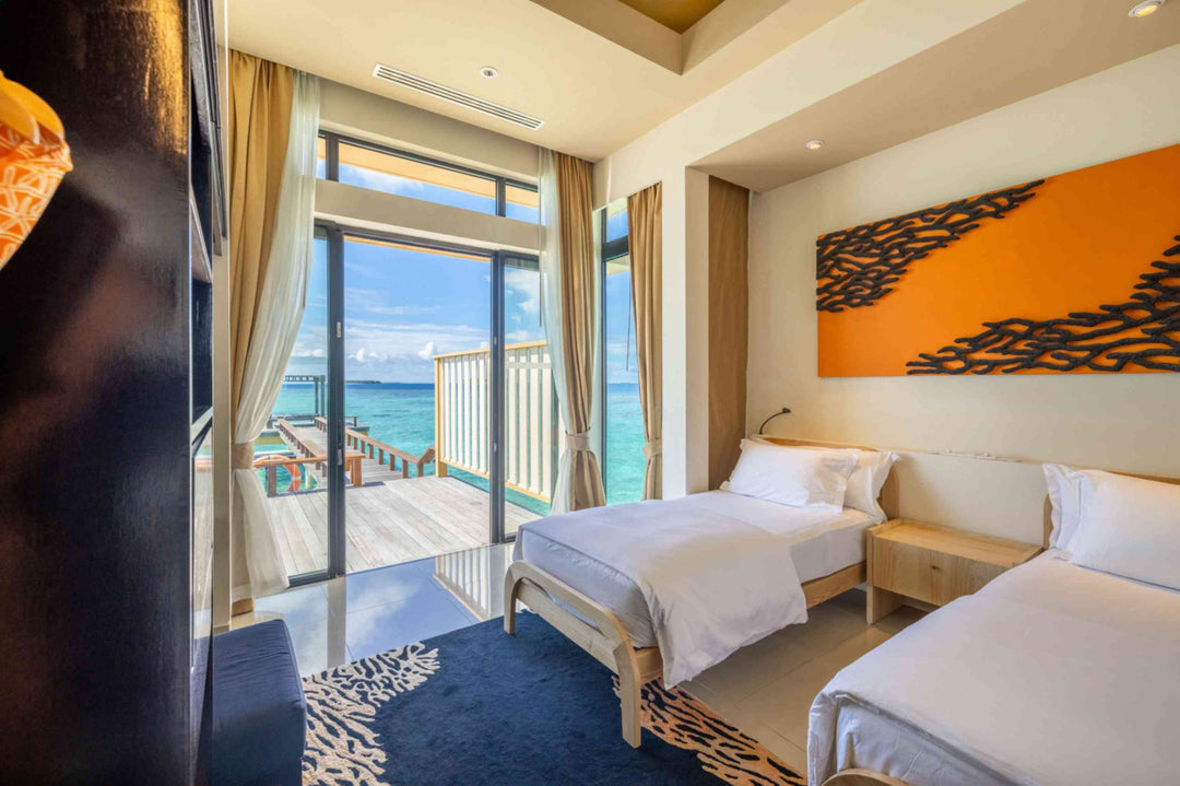 Angsana Velavaru, Dhaalu Atoll — twin beds in the second bedroom of the overwater villa, under orange coral artwork