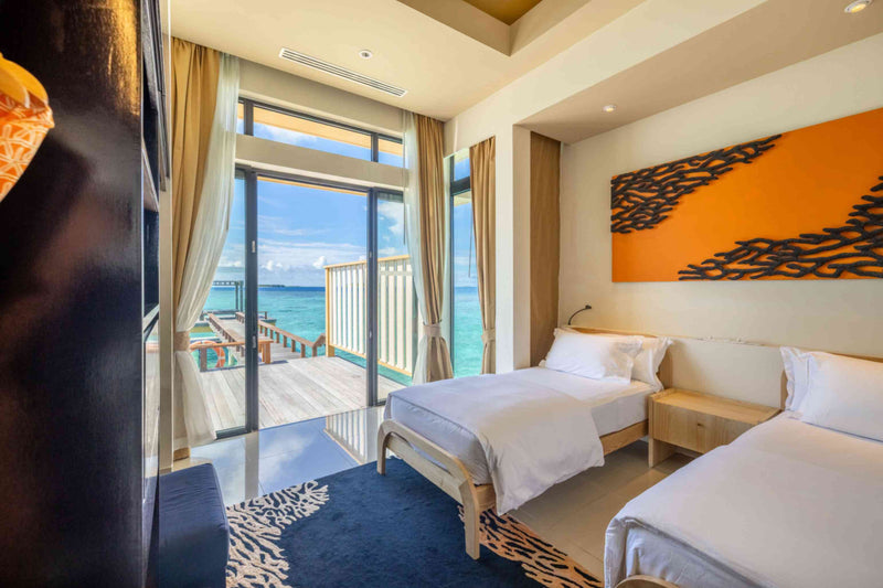 Twin beds in the second bedroom of the overwater villa at Angsana Velavaru, under orange coral artwork.