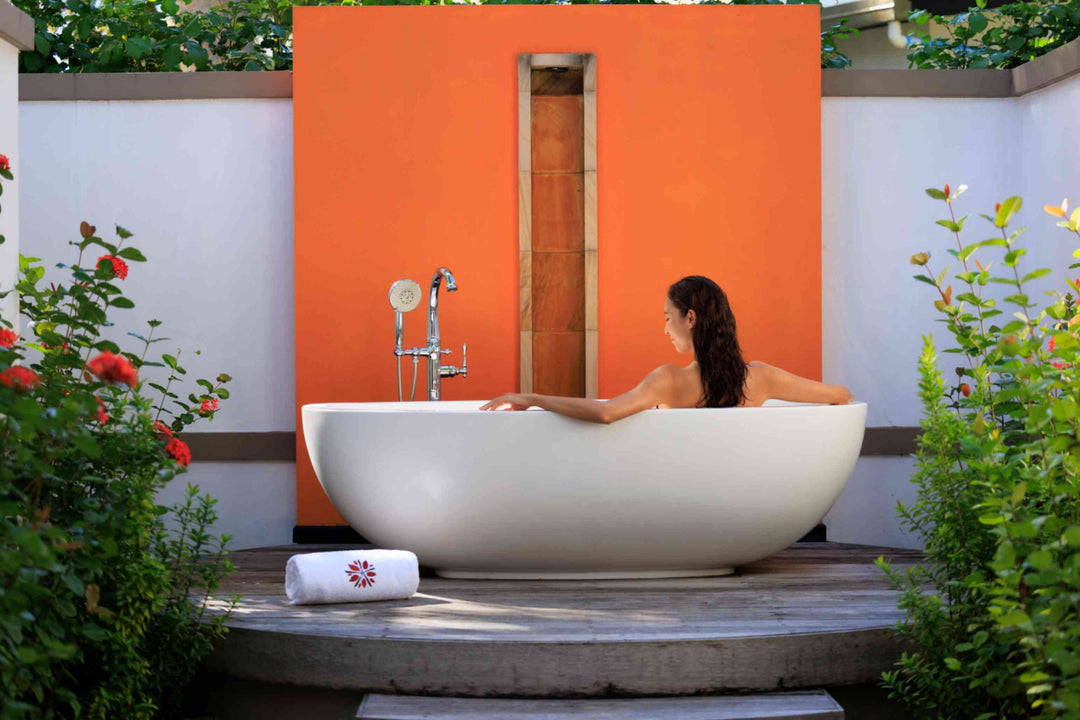 Angsana Velavaru, Dhaalu Atoll — a guest in the freestanding outdoor bathtub, set against an orange garden wall