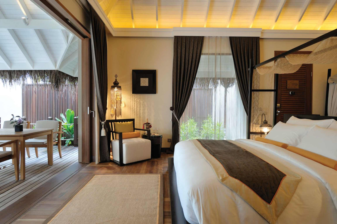 A beach villa bedroom at Ayada Maldives, four poster bed and writing desk opening to the deck