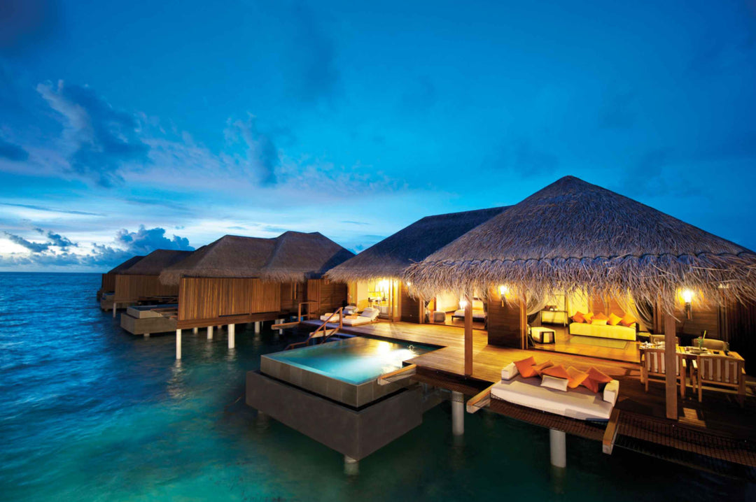 Overwater suites at Ayada Maldives lit at dusk, plunge pools glowing above the lagoon
