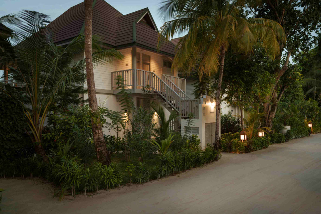 Sun Siyam Olhuveli, South Malé Atoll — two-storey Beach Pavilion block lit at dusk, with palms and a sand path