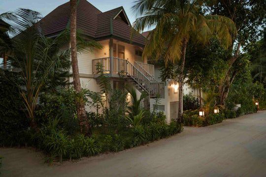 Sun Siyam Olhuveli, South Malé Atoll — two-storey Beach Pavilion block lit at dusk, with palms and a sand path