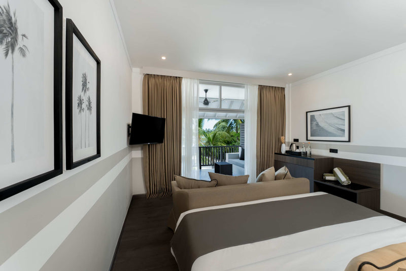 A first-floor Beach Pavilion bedroom at Sun Siyam Olhuveli with a king bed, framed palm prints and a balcony.