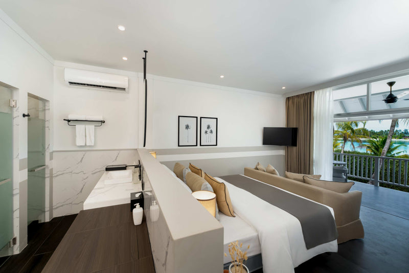 A first-floor Beach Pavilion bedroom at Sun Siyam Olhuveli with the bathroom open behind the bed and doors to the balcony.