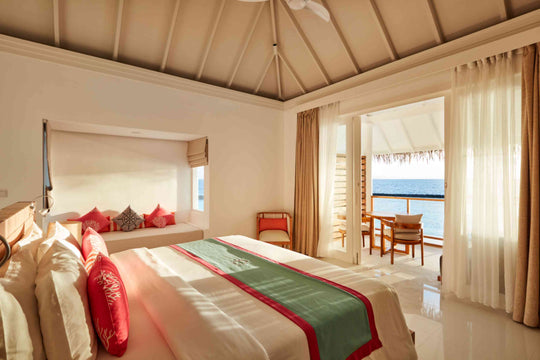 Sun Siyam Iru Veli, Dhaalu Atoll — villa bedroom under a vaulted timber ceiling, doors open to a deck and the lagoon