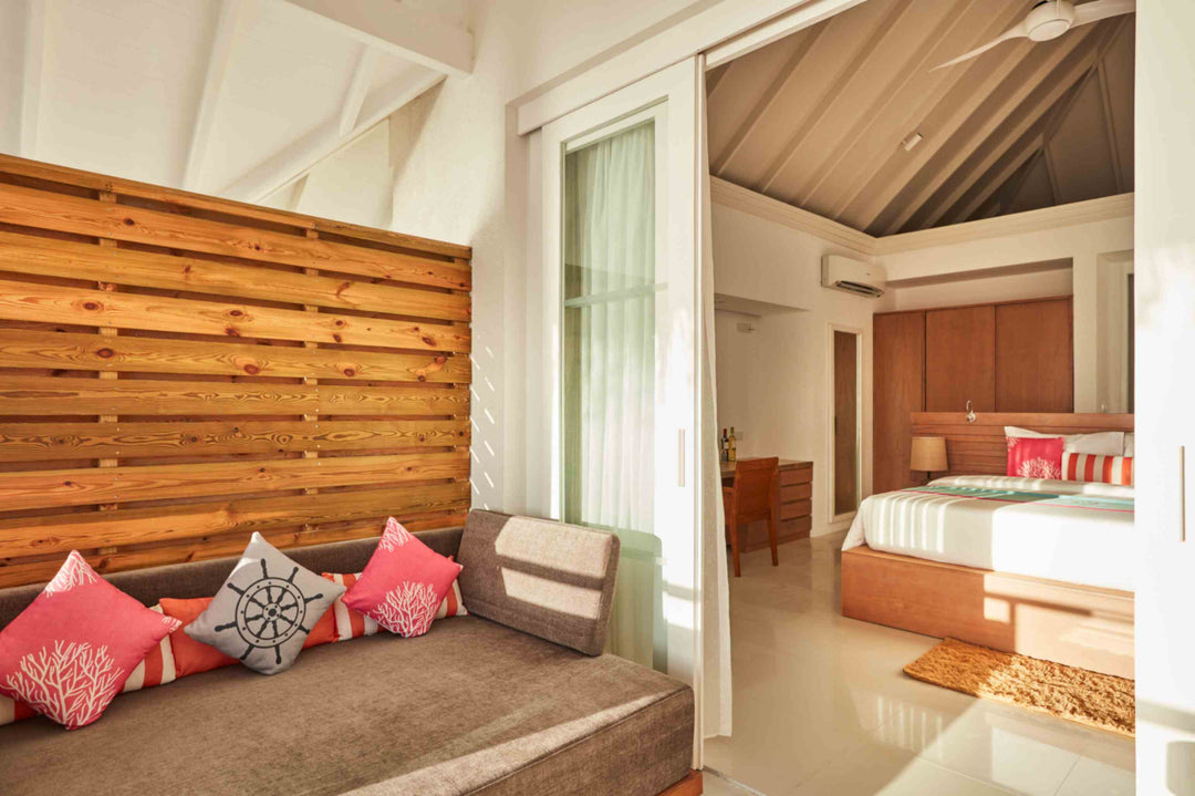 Sun Siyam Iru Veli, Dhaalu Atoll — living area with a timber slat screen, sofa with coral cushions and the bedroom beyond