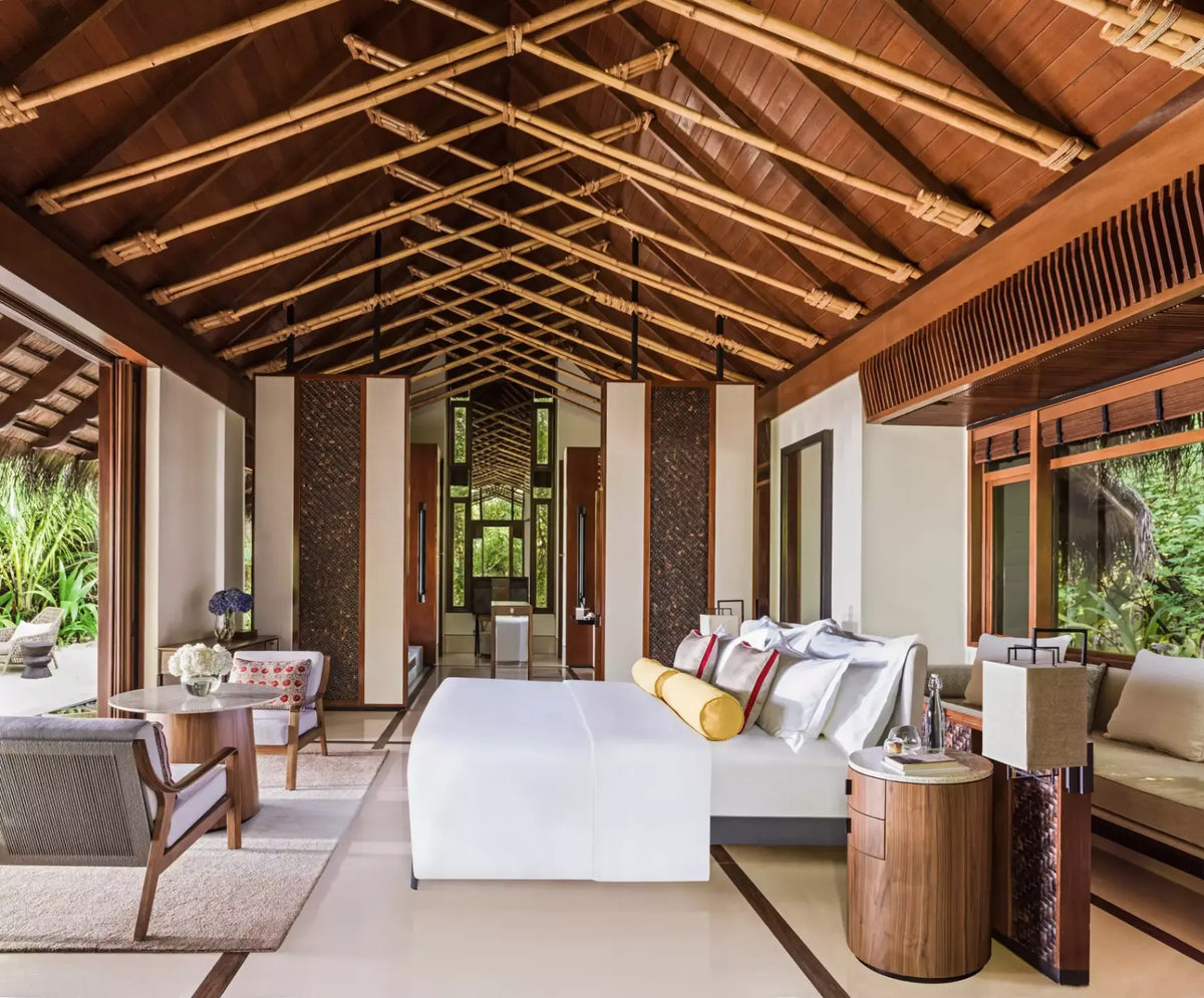 One&Only Reethi Rah Beach Villa bedroom, a king bed under a high timber and thatch ceiling with doors open to tropical garden