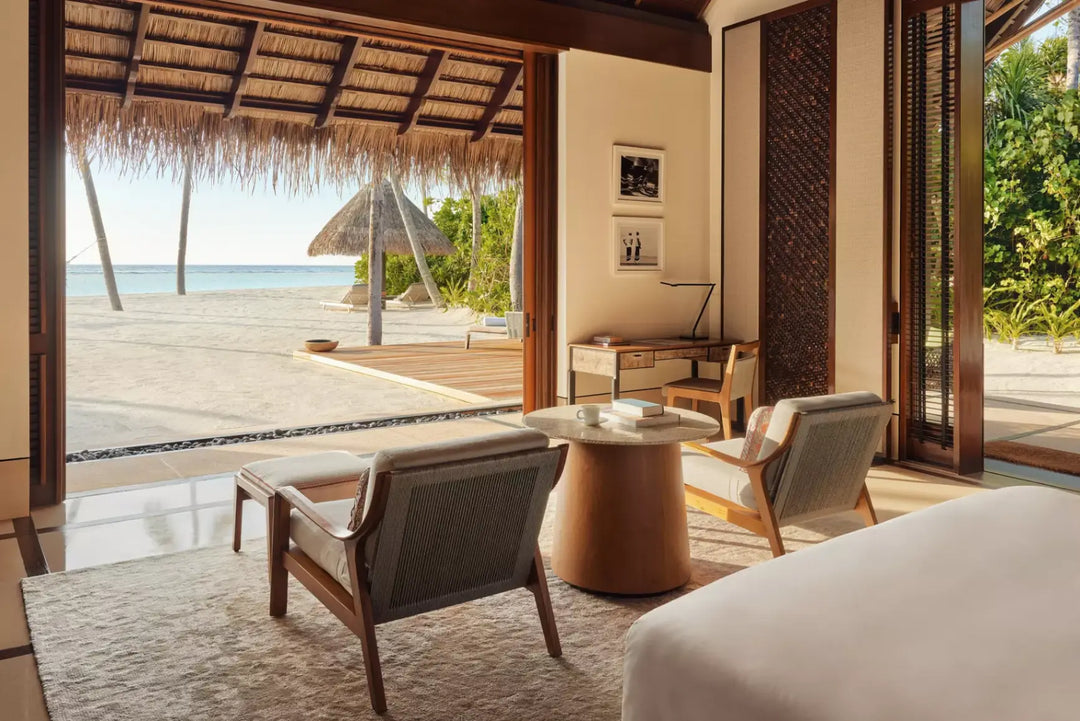 View out from a One&amp;Only Reethi Rah Beach Villa to its private beach, with sun loungers under a thatched parasol and turquoise water beyond