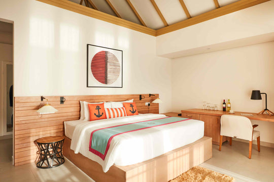Sun Siyam Iru Veli, Dhaalu Atoll — bedroom with a timber slat headboard, orange anchor cushions and a writing desk
