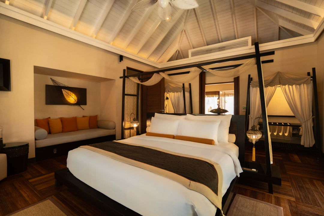A four poster bed at Ayada Maldives flanked by two nightstands under a timber ceiling